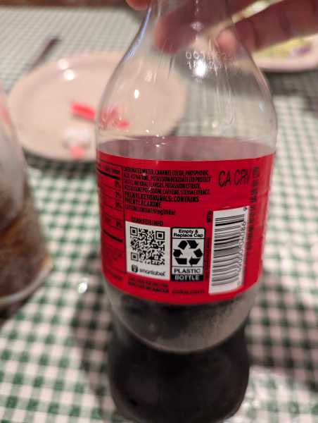A Coca-Cola Zero Sugar bottle turned to show the ingredients label which reads: Carbonated Water, Caramel Color, Phosphoric Acid, Aspartame, Potassium Benzoate (to protect flavor), Natural Falvors, Potassium Citrate, Acesulfate Potassium, Caffeine, Stevia Extract. Phenylketonurics: Contains Phenylalanine. Caffeine Content: 57mg/20 fl oz